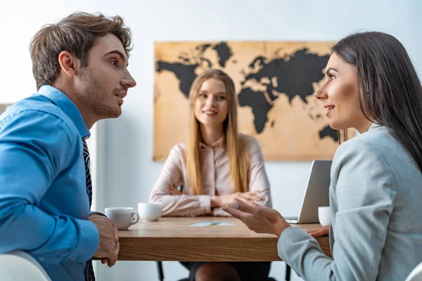 Selective focus of smiling travel agent looking at disputing couple of tourists — Stock Photo