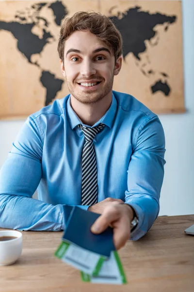 Selective focus of travel agent looking at camera while holding passports and air tickets — Stock Photo