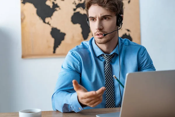 Agente de viajes desalentado en auriculares que trabajan cerca de la computadora portátil - foto de stock