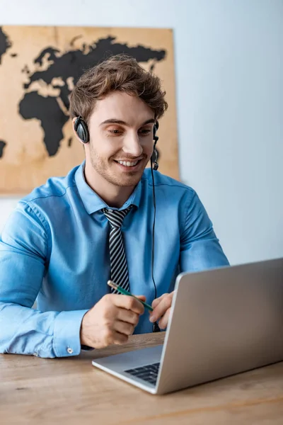 Agente de viajes sonriente en auriculares mirando portátil - foto de stock