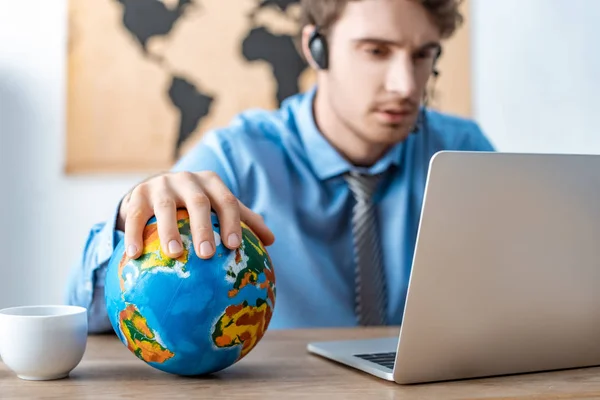 Selective focus of travel agent touching globe while working near laptop — Stock Photo