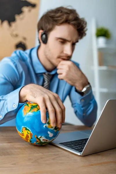 Selective focus of thoughtful travel agent touching globe while sitting at workplace — Stock Photo