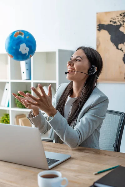 Cheerful travel agent playing with globe at workplace — Stock Photo