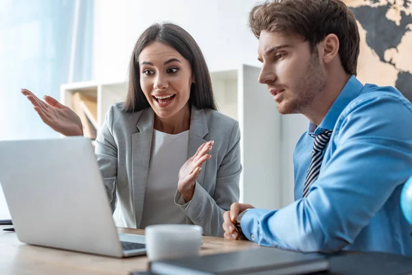 Aufgeregtes Reisebüro zeigt Wow-Geste beim Blick auf Laptop-Bildschirm zusammen mit nachdenklicher Kundin — Stockfoto