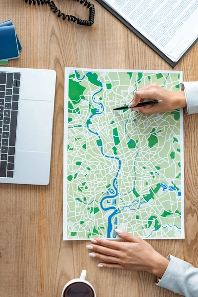 Cropped view of travel agent pointing with pen at map on wooden desk — Stock Photo