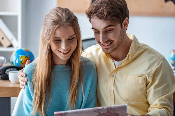 Happy couple of tourists looking at map in travel agency — Stock Photo