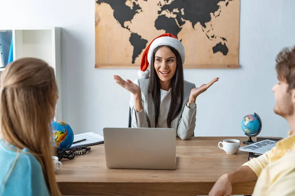 Alegre agente de viajes en santa hat hablando con un par de turistas - foto de stock