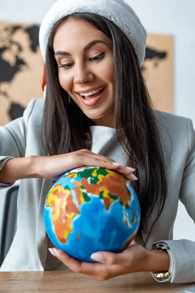 Feliz agente de viajes celebración globo mientras está sentado en el lugar de trabajo - foto de stock