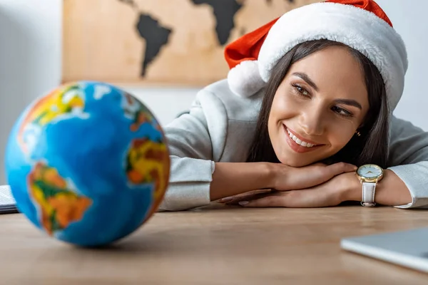 Smiling travel agent looking at globe while sitting at workplace — Stock Photo