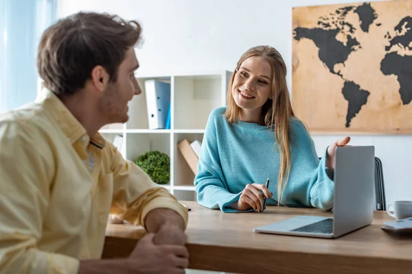 Agente de viajes sonriente apuntando a la pantalla del ordenador portátil mientras habla con el cliente - foto de stock