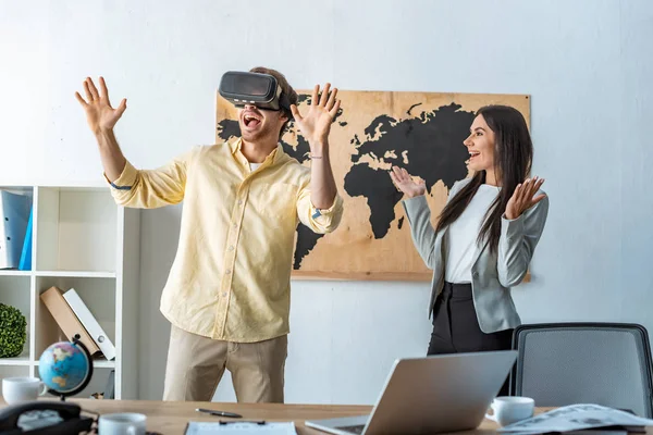 Agent de voyage souriant regardant l'homme excité en utilisant vr casque — Photo de stock