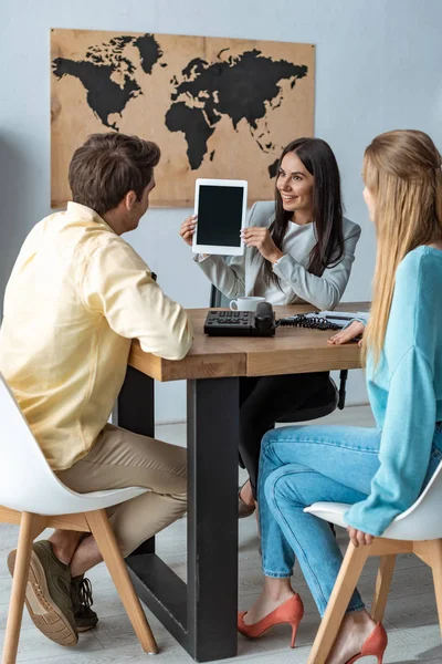 Sonriente agente de viajes mostrando tableta digital a un par de turistas - foto de stock