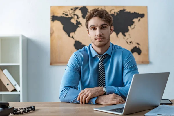 Fiducioso agente di viaggio guardando la fotocamera mentre seduto sul posto di lavoro — Foto stock