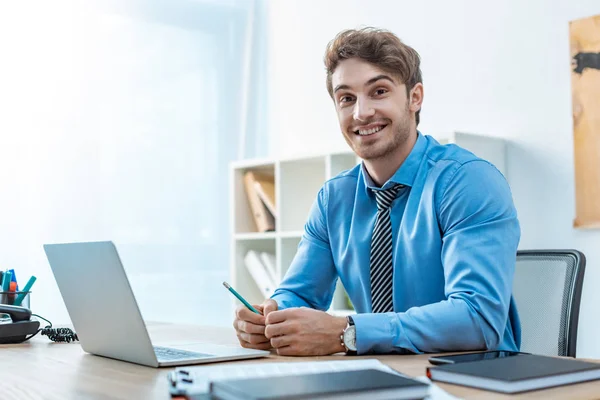 Cheerful travel agent looking at camera while sitting at workplace — Stock Photo