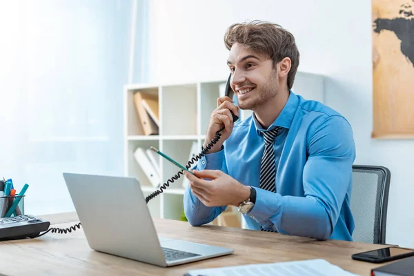 Smiling travel agent talking on phone while holding pencil — Stock Photo