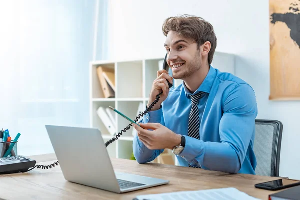 Agent de voyage souriant parlant au téléphone tout en tenant un crayon — Photo de stock