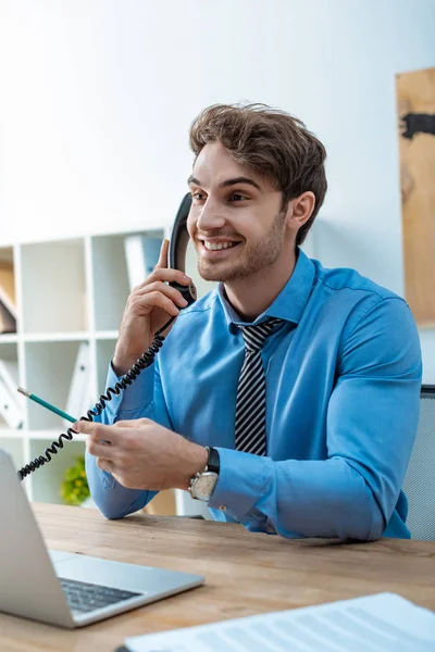 Cheerful travel agent talking on phone while holding pencil — Stock Photo