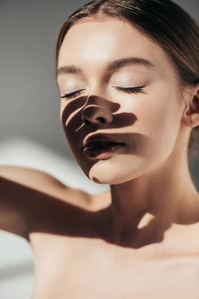 Porträt eines nackten Mädchens mit geschlossenen Augen und Schatten im Gesicht auf grau — Stockfoto