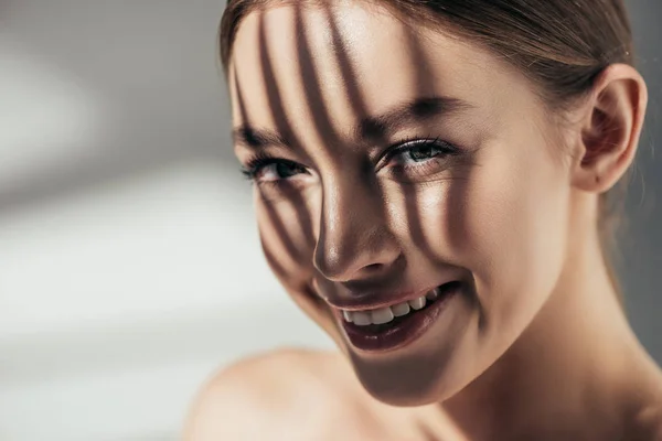 Porträt eines lächelnden Mädchens mit Schatten im Gesicht auf grau — Stockfoto