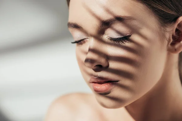 Porträt eines attraktiven nackten Mädchens mit geschlossenen Augen und Schatten auf dem Gesicht auf grau — Stockfoto