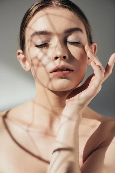 Portrait de fille nue tendre avec les yeux fermés et les ombres sur le visage sur gris — Photo de stock