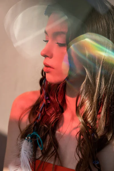 Tierna chica boho con trenzas en peinado posando en luz roja con bengalas de lente - foto de stock