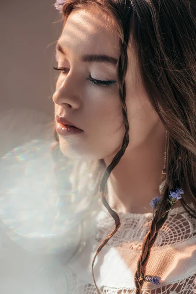 Tierna chica con trenzas en peinado posando en vestido boho blanco sobre gris con bengalas de lente - foto de stock