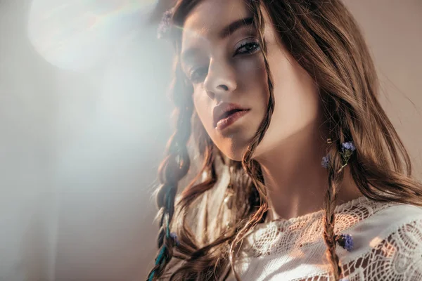 Attractive bohemian girl with braids in hairstyle posing in white boho dress on grey with lens flares — Stock Photo