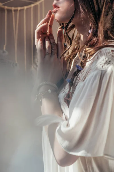 Cropped view of girl with braids in hairstyle posing in white boho dress on grey with lens flares — Stock Photo