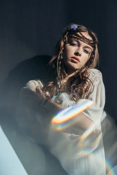 Menina atraente com tranças no penteado posando em vestido de boho branco no cinza com flares de lente — Fotografia de Stock