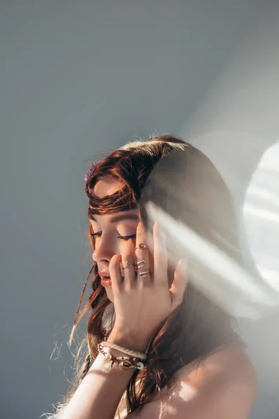 Нежная обнаженная девушка с косичками в прическе, позирующая на сером с бликами от объектива — стоковое фото