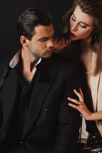 Atractiva mujer abrazando guapo hombre en traje aislado en negro — Stock Photo
