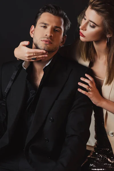 Atractiva mujer abrazando guapo hombre en traje aislado en negro - foto de stock