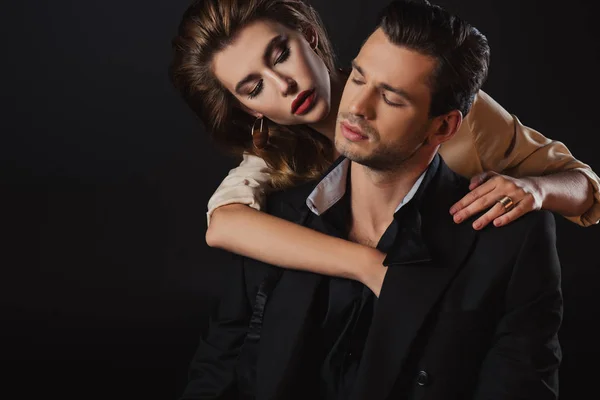Attraktive Frau umarmt gutaussehenden Mann im Anzug isoliert auf schwarz — Stockfoto