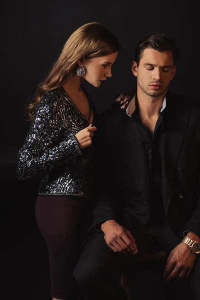 Attractive woman holding tie of handsome man in suit isolated on black — Stock Photo