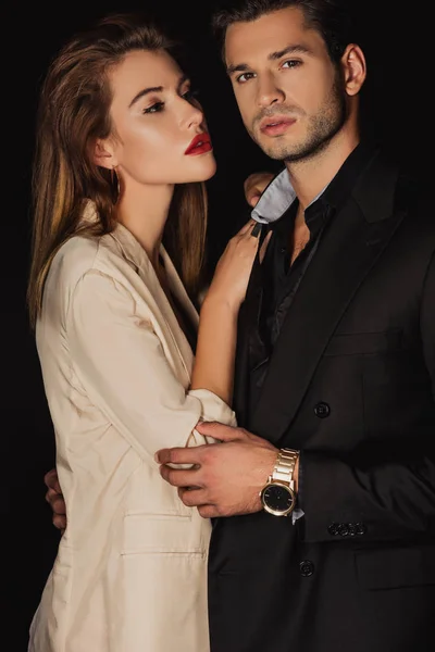 Atractiva mujer abrazando guapo hombre en traje aislado en negro - foto de stock