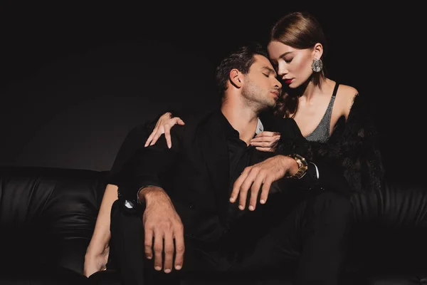 Vista de ángulo bajo de la mujer atractiva abrazo y besos hombre guapo aislado en negro - foto de stock
