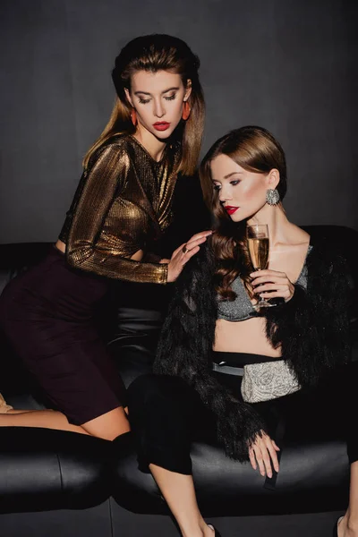 Séduisantes et élégantes femmes avec verre champagne sur canapé isolé sur noir — Photo de stock
