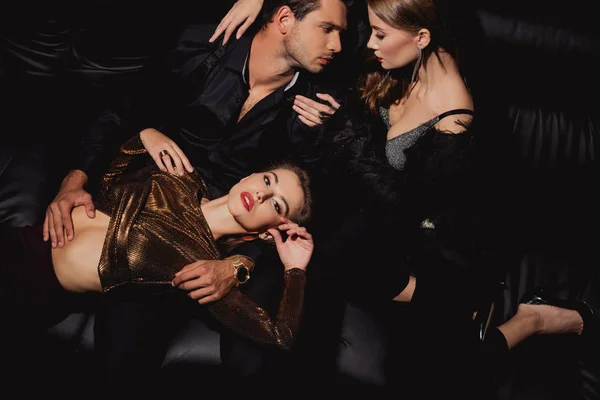 Vue de dessus des femmes attrayantes couché et étreignant bel homme isolé sur noir — Photo de stock