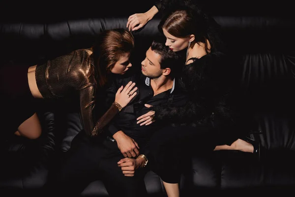 Top view of attractive women kissing and hugging handsome man on black background — Stock Photo