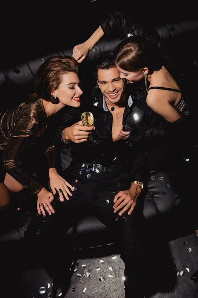 Top view of attractive and smiling women and handsome man with champagne glass on black background — Stock Photo