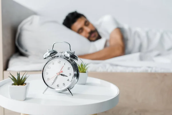 Selective focus of alarm clock, plants and handsome bi-racial man sleeping on background — Stock Photo