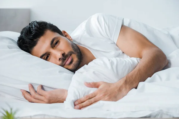 Красивый двурасовый мужчина лежит в постели и смотрит в камеру утром. — стоковое фото