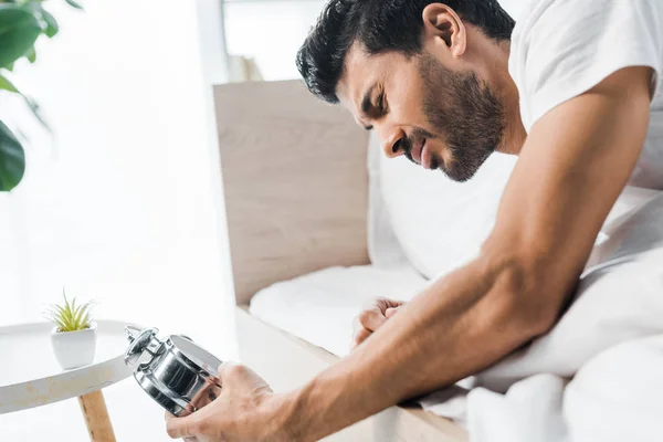 Красивий бі-расовий чоловік тримає будильник і прокидається вранці — стокове фото