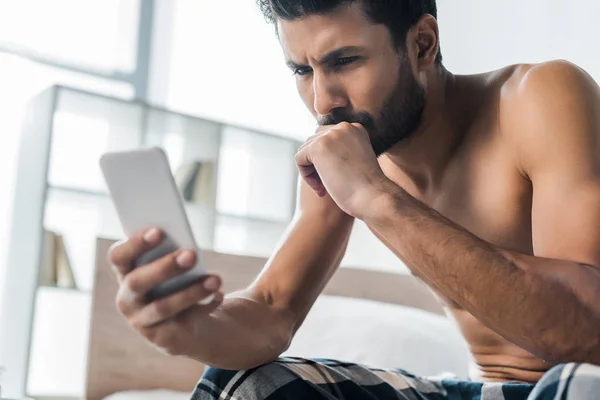 Messa a fuoco selettiva di pensoso e sexy uomo bi-razziale utilizzando smartphone al mattino — Foto stock