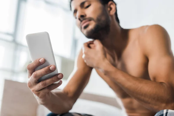 Enfoque selectivo de hombre bi-racial guapo y sexy usando teléfono inteligente en la mañana - foto de stock