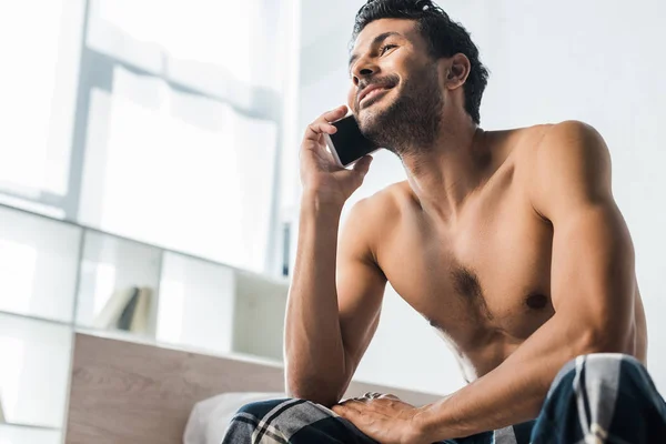 Vista de ángulo bajo del hombre bi-racial guapo y sonriente hablando en el teléfono inteligente en la mañana - foto de stock