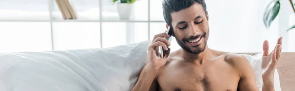 Plano panorámico de hombre bi-racial guapo y sonriente hablando en el teléfono inteligente en la mañana - foto de stock