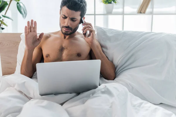 Красивый двурасовый мужчина с ноутбуком разговаривает на смартфоне утром — стоковое фото