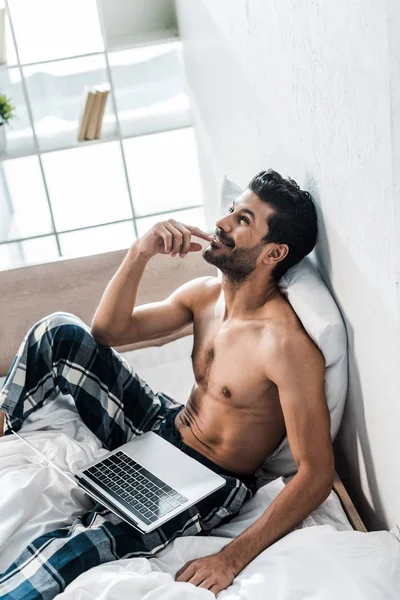 Высокий угол обзора красивого и улыбающегося двурасового мужчины с ноутбуком утром — стоковое фото